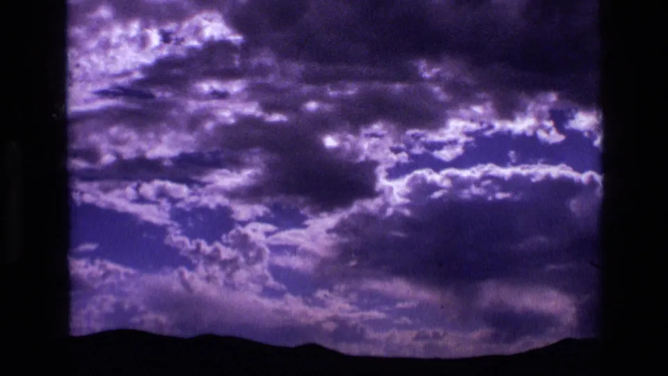 1972 Idaho home-movie frame of purple cloud formations above a dark mountain ridge.