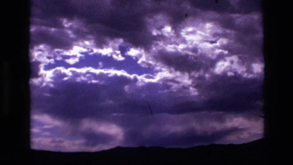 1972 Idaho 8mm frame showing textured purple clouds across the sky with a dark mountainous ridge along the bottom edge.