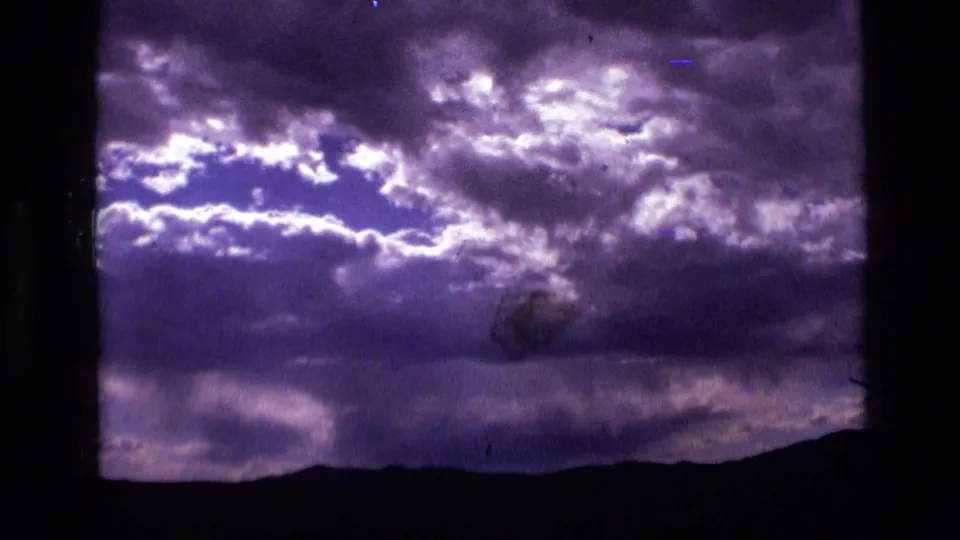 1972 Idaho 8mm frame with luminous breaks in dense clouds above a silhouetted mountain horizon and visible film wear.