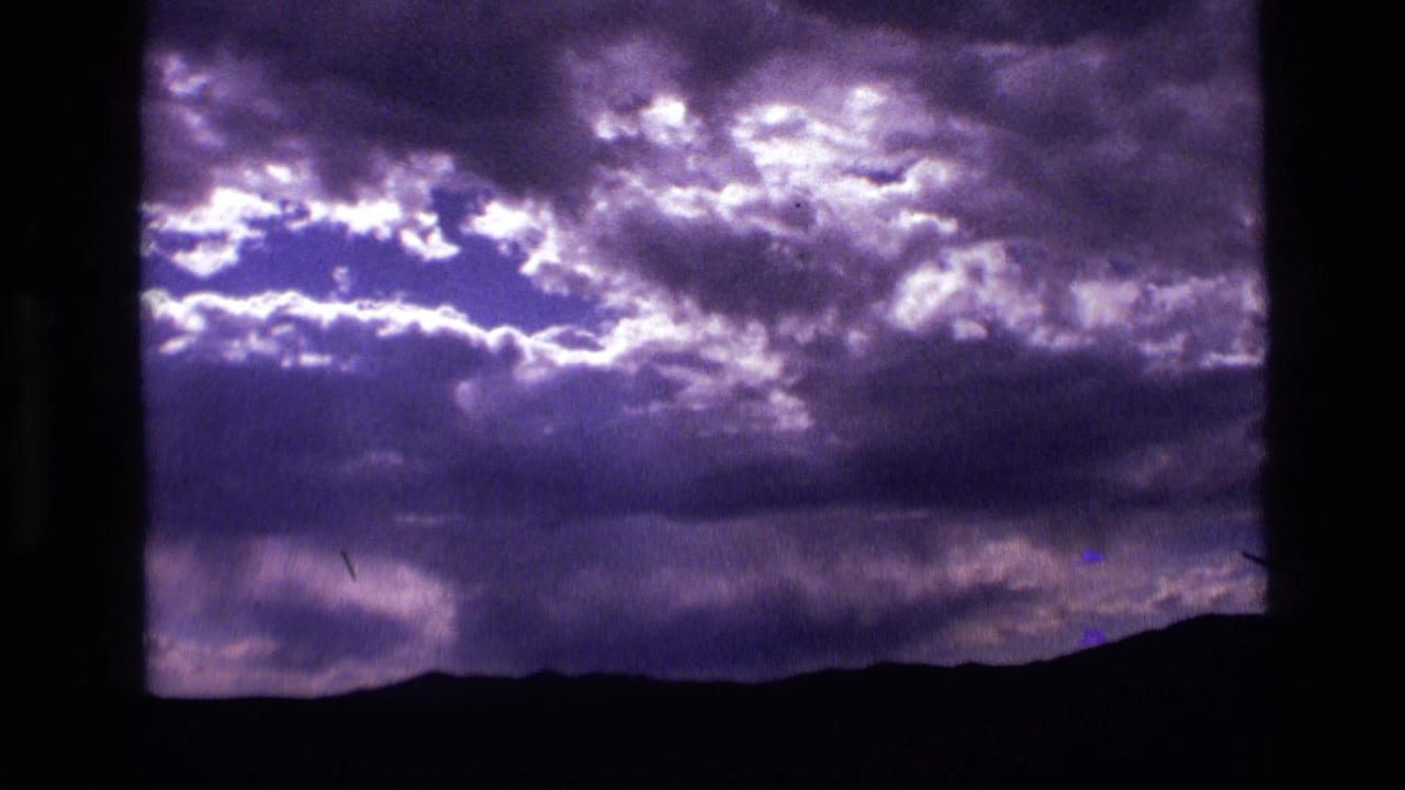 1972 Idaho 8mm frame showing violet storm clouds above a dark distant hill line, with bright gaps in the cloud cover.