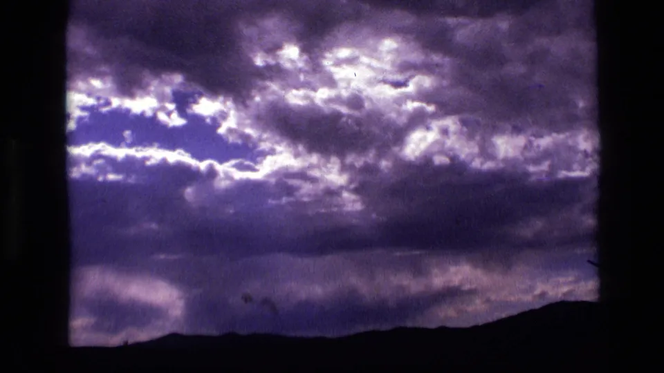 1972 Idaho 8mm frame showing layered purple storm clouds over a dark ridge, with grain and color shift from the film scan.