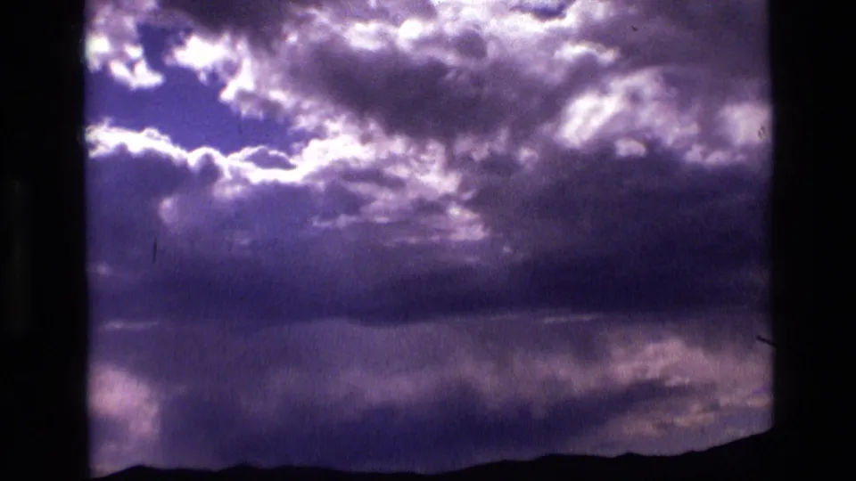 1972 Idaho 8mm frame with a bright opening in violet cloud cover above a dark low mountain silhouette.