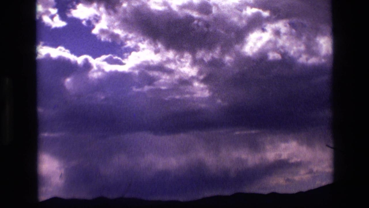 1972 Idaho 8mm frame showing sunlit clouds in a purple-gray sky above a low dark landscape silhouette.
