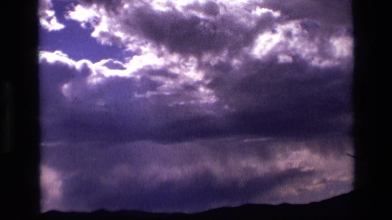1972 Idaho 8mm frame with dense highlighted clouds, purple sky tones, and a dark low horizon line.