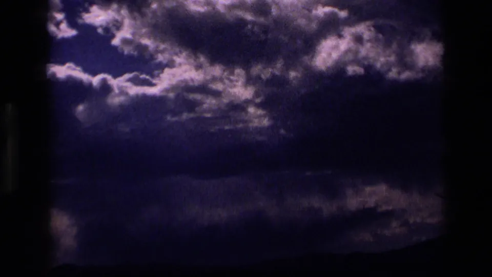 1972 Idaho 8mm frame showing a darker exposure of clouds and sunlight over a nearly black horizon.