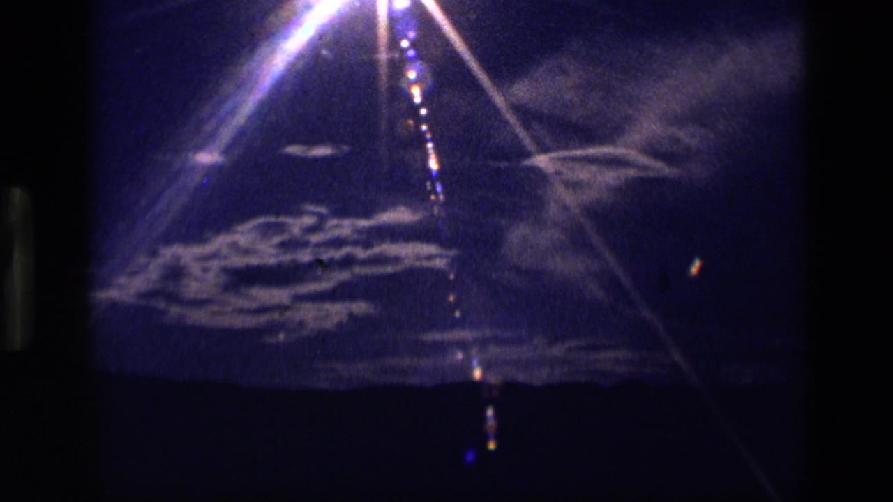 Bright sun flare over a dark mountain horizon with white clouds in a blue-purple sky.