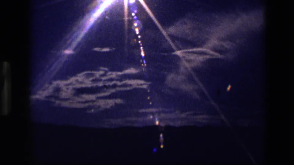 1972 Idaho 8mm frame showing intense sunlight, white cloud bands, lens streaks, and a dark mountain silhouette.