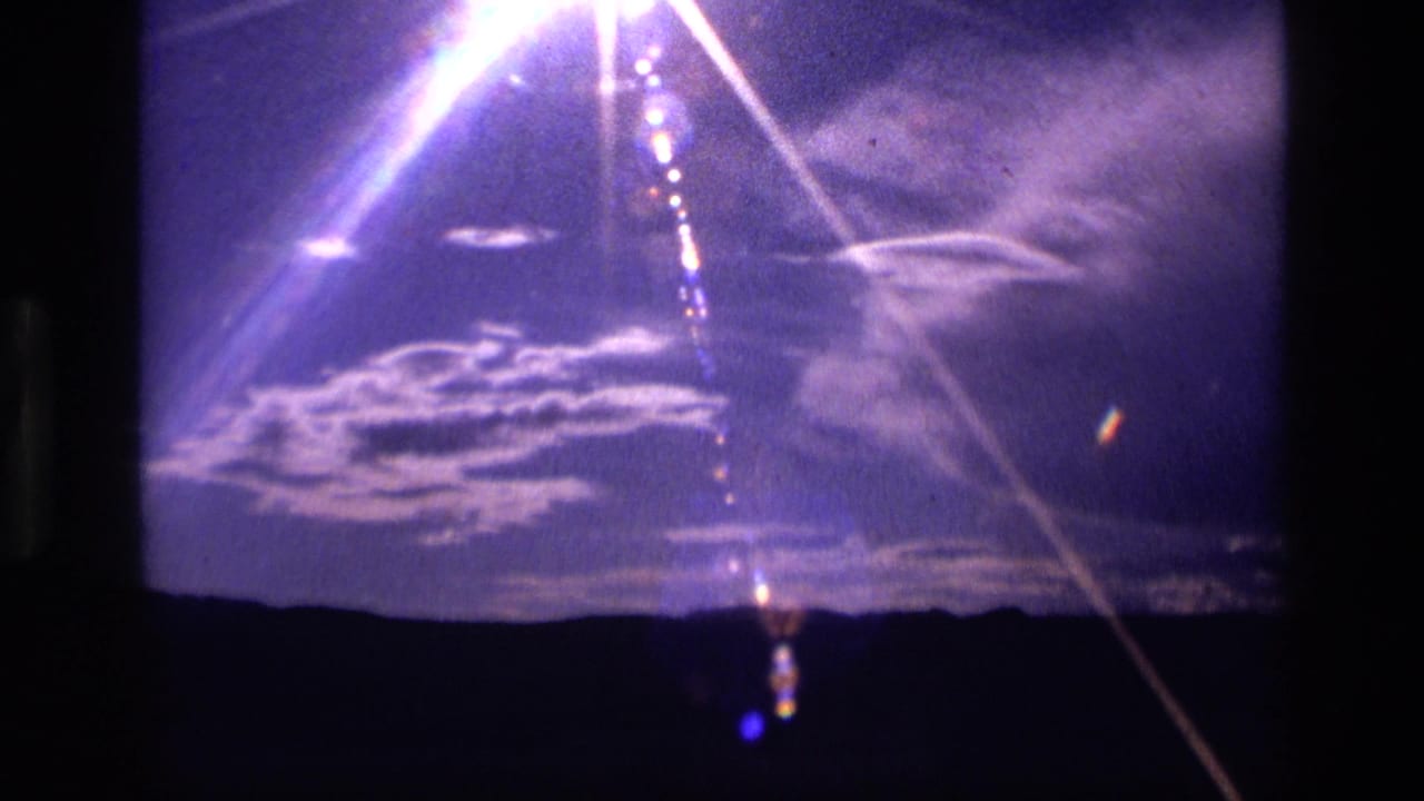 1972 Idaho 8mm view of cloud formations and strong optical flare above a silhouetted mountain horizon.