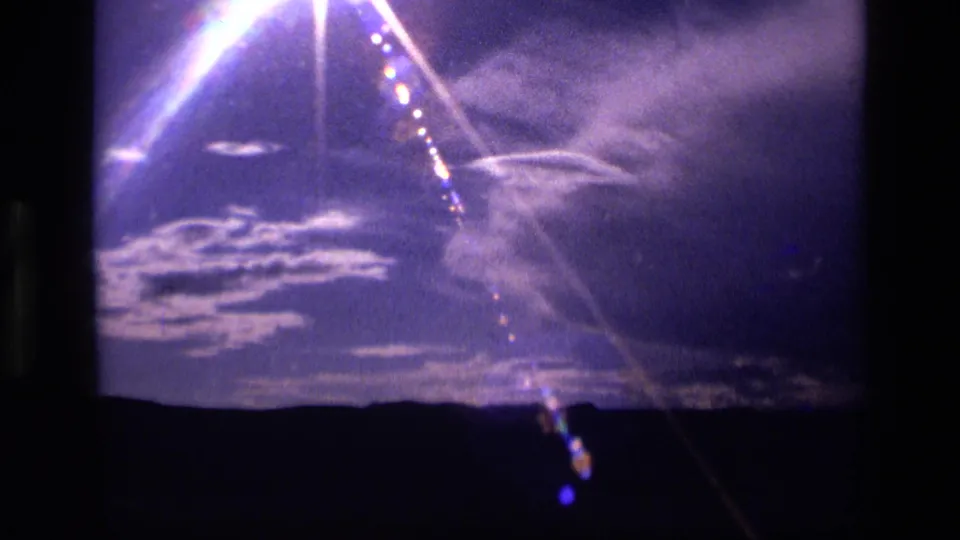 1972 Idaho home-movie frame with bright glare, layered white clouds, and a dark landscape edge below.
