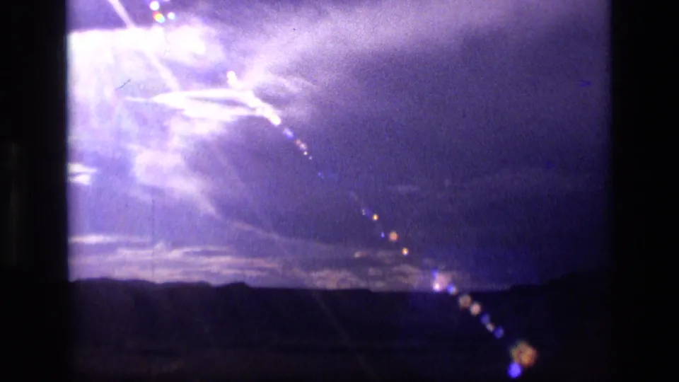 1972 Idaho 8mm frame showing a silhouetted horizon beneath a purple-blue sky, with strong glare, clouds, and lens flare.