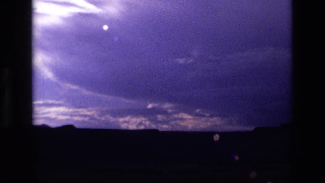 Dark landscape under a purple sky with clouds and a small bright point.
