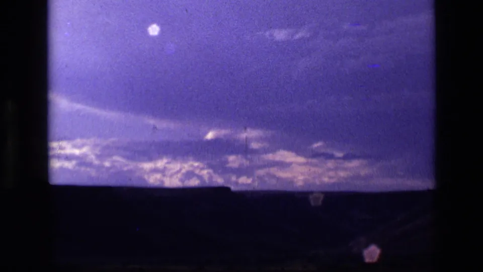 1972 Idaho 8mm frame showing a broad purple-blue cloud field over a silhouetted landscape, with faint flare and grain.