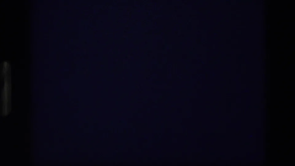 Underexposed 8mm frame from the Idaho sky sequence, with little visible beyond dark blue-purple film texture.