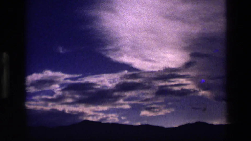1972 Idaho 8mm frame showing a luminous cloud mass above dark ridgeline silhouettes in a purple dusk sky.