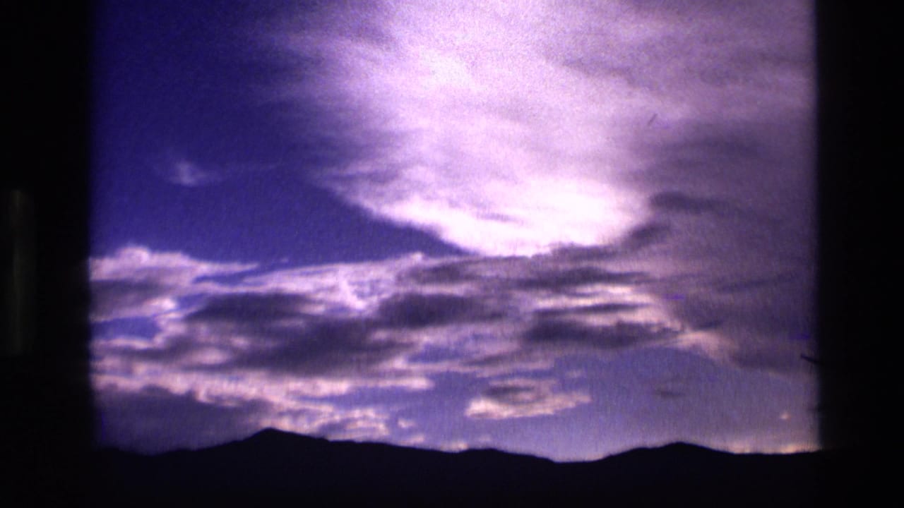 1972 Idaho 8mm frame showing layered twilight clouds above a dark mountain silhouette, with purple-blue color and visible film grain.