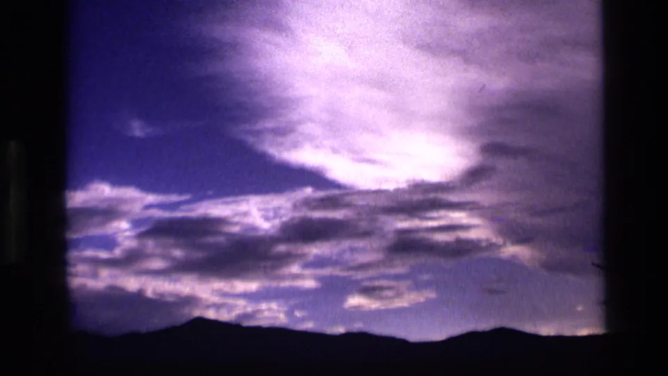 1972 Idaho 8mm frame showing layered twilight clouds above a dark mountain silhouette, with purple-blue color and visible film grain.