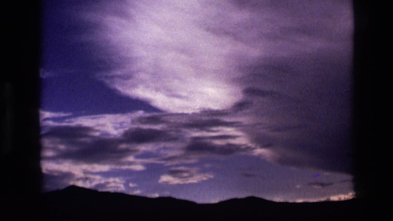 1972 Idaho 8mm frame with drifting clouds and a dark mountain horizon under a blue-purple evening sky.