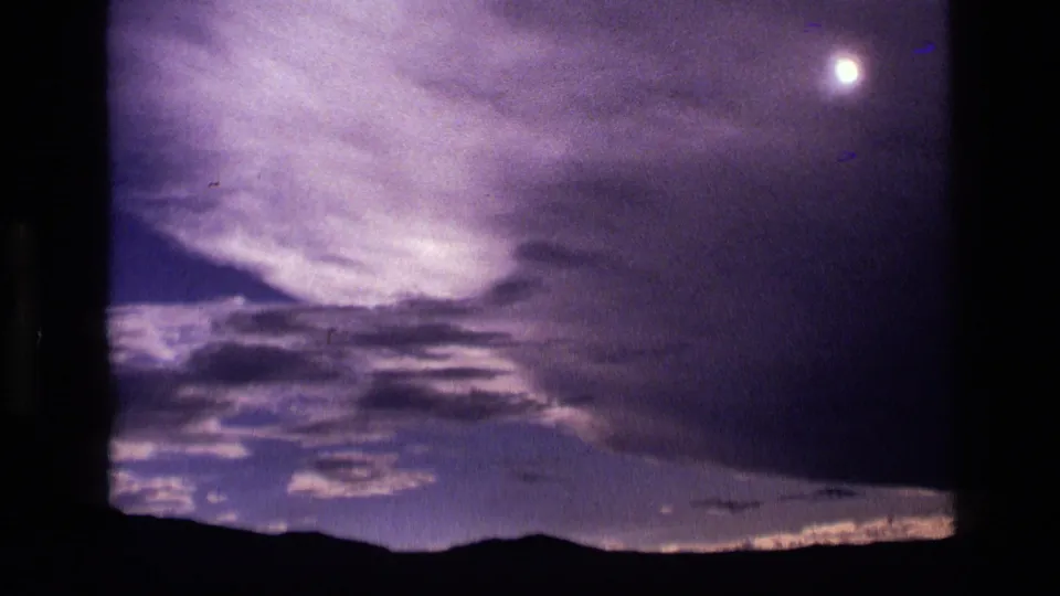 1972 Idaho 8mm frame showing the moon in the upper sky, clouds below it, and a silhouetted mountain horizon.