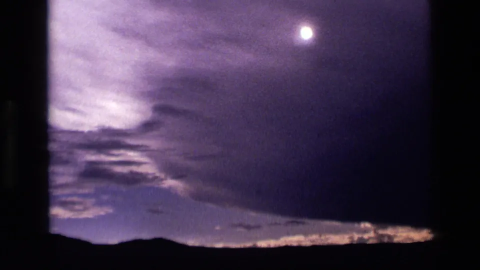 1972 Idaho 8mm frame with a bright moon, soft clouds, and a dark mountain silhouette beneath the twilight sky.
