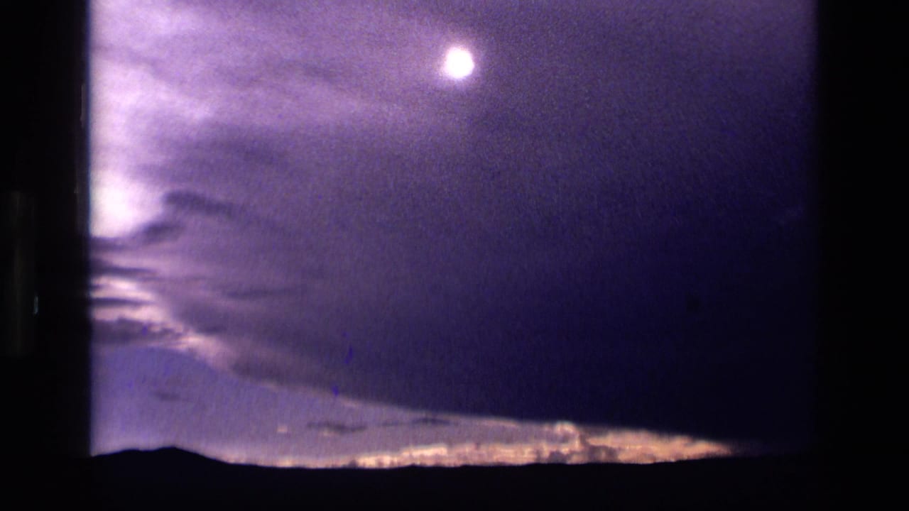 Bright moon shining through purple clouds over a dark low horizon.