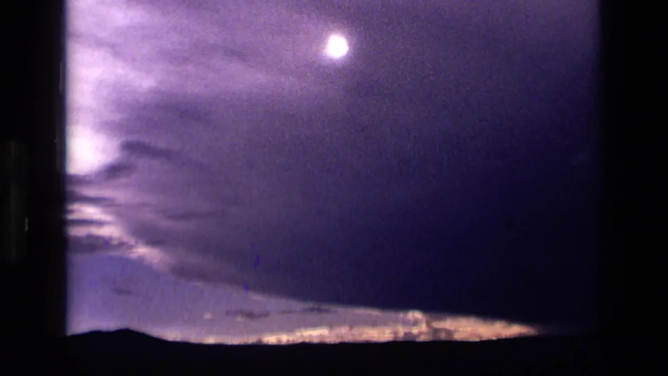 1972 Idaho 8mm frame with the moon near the upper sky, purple cloud cover, and a thin glowing horizon line.