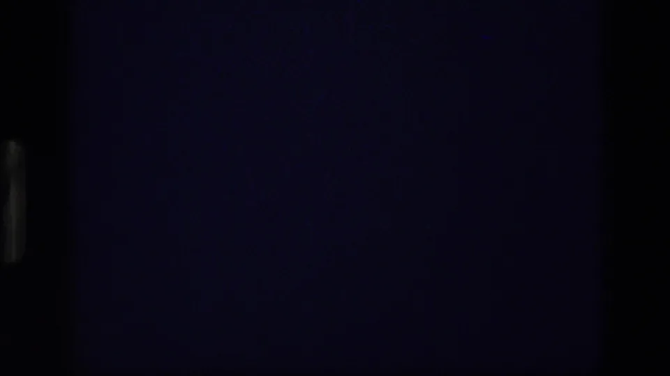 Dark 8mm frame from the 1972 Idaho night-sky clip, with most of the view underexposed and only faint blue-purple tonal variation visible.
