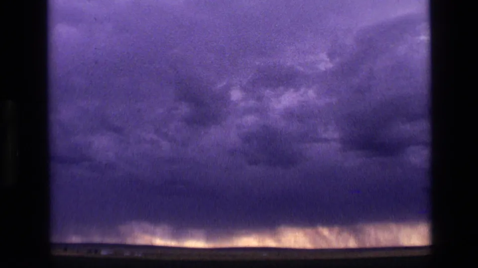 1972 Idaho 8mm frame showing dense purple-blue cloud cover above a faintly glowing low horizon at night.