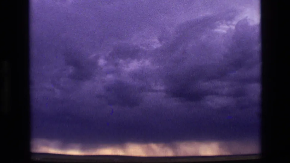 1972 Idaho 8mm frame showing heavy storm clouds above a faintly lit flat horizon, tinted purple and blue by the film stock.