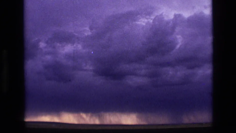 1972 Idaho 8mm frame with a broad, dark cloud mass and faint vertical streaks near the horizon that may be distant rain.