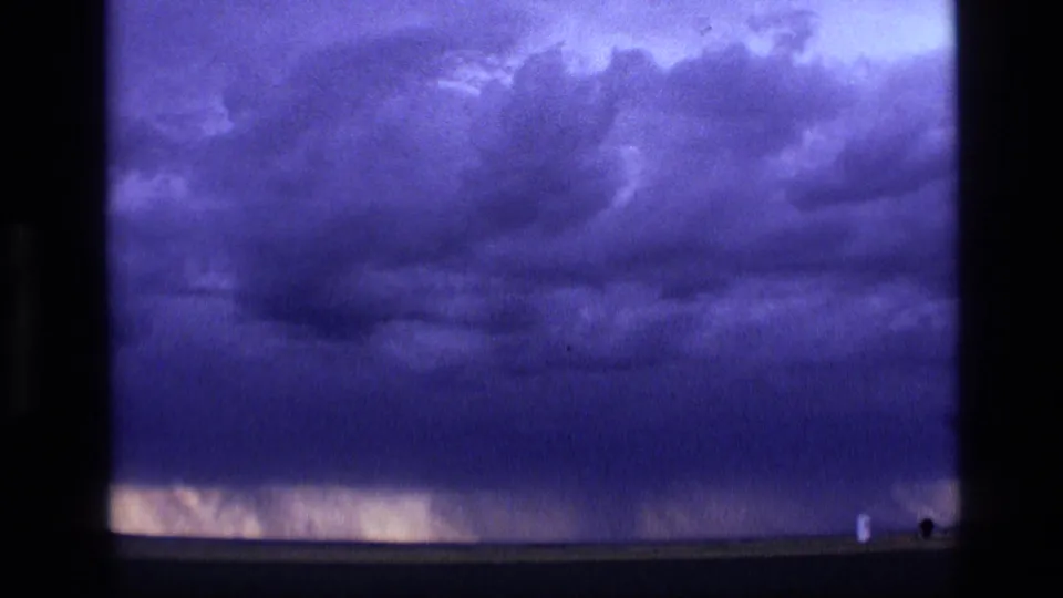 1972 Idaho 8mm frame showing layered storm clouds filling most of the sky, with a narrow pale glow along the lower horizon.