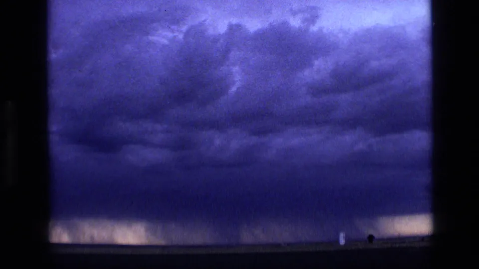 1972 Idaho 8mm frame showing an expansive dark storm sky over a flat horizon, with small dark marks near the lower right edge.