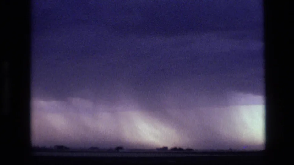 1972 Idaho 8mm frame showing dark purple storm clouds above a low horizon and bright rain shaft in the distance.