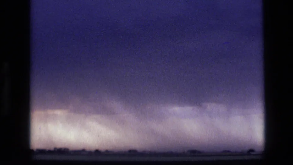 1972 Idaho 8mm view of a broad storm front, with muted blue-purple sky and a light rain band near the horizon.