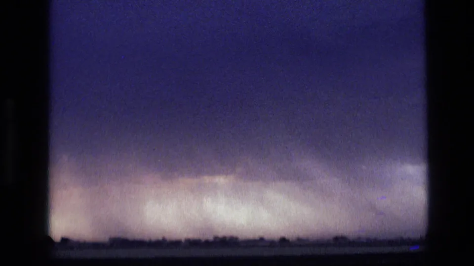 1972 Idaho frame showing a dark rural horizon under broad purple clouds and a luminous rain band in the distance.