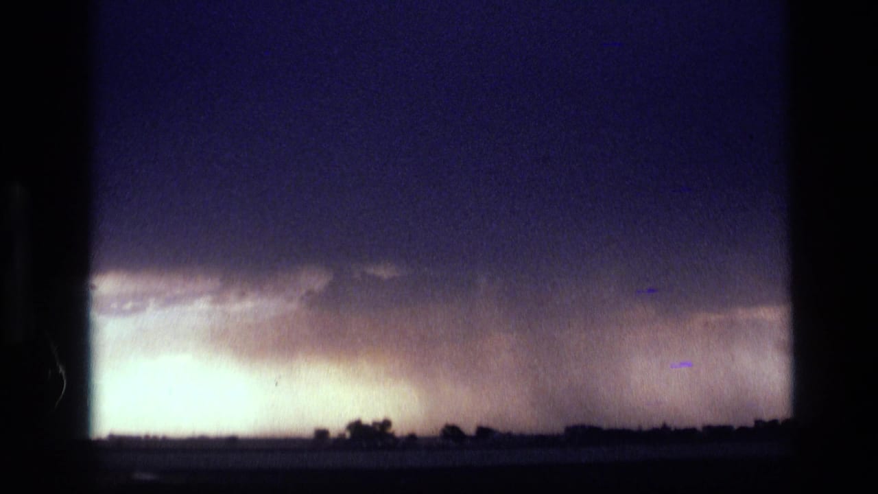 1972 Idaho 8mm frame with a bright rain curtain beneath a dark cloud shelf over a distant flat landscape.