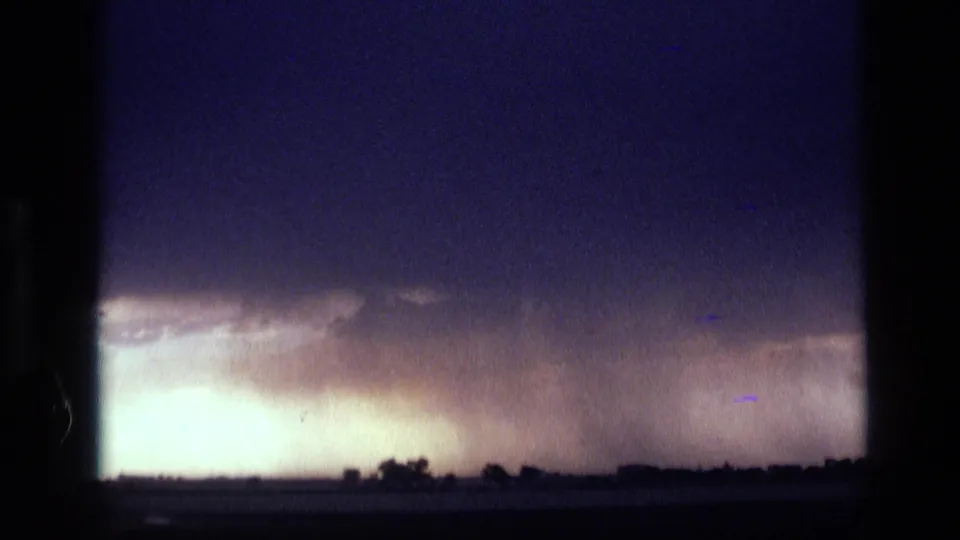 1972 Idaho 8mm frame with a bright rain curtain beneath a dark cloud shelf over a distant flat landscape.