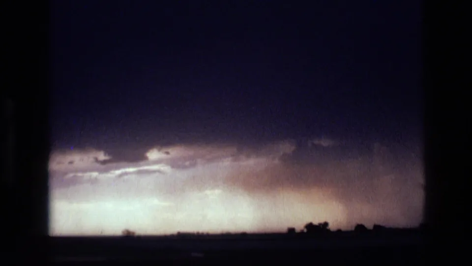 1972 Idaho 8mm frame showing pale storm light and layered clouds above a flat rural horizon.