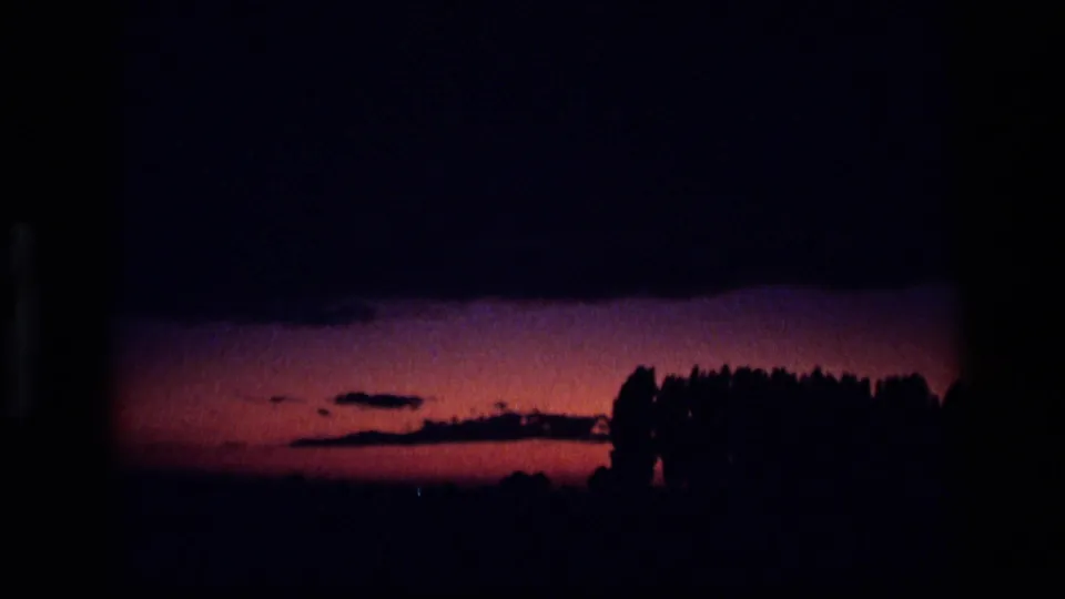 1972 Idaho 8mm frame showing an orange-pink sunset beneath dark clouds, with trees silhouetted on the horizon.