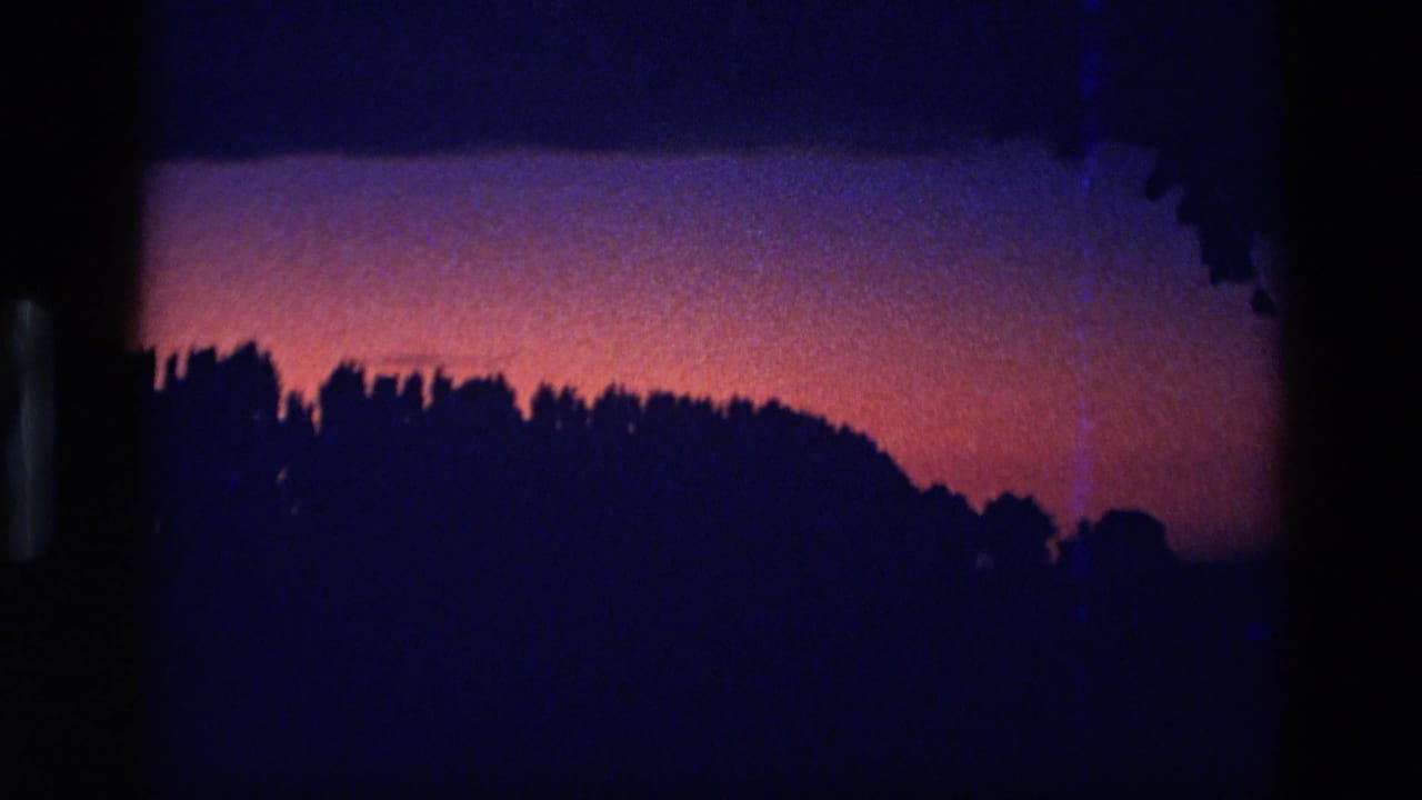 1972 Idaho home-movie still with a dark forested ridge cutting across a red and purple twilight horizon.