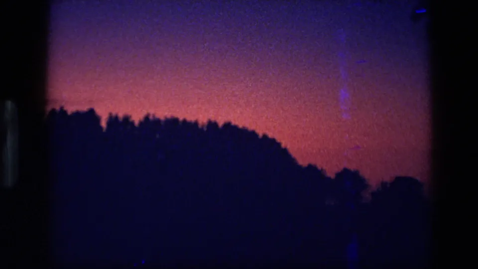 1972 Idaho 8mm frame showing a magenta dusk or dawn sky over a black treeline and rounded hill profile.