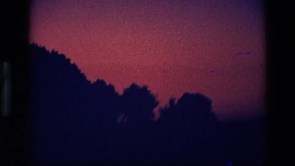 1972 Idaho home-movie frame with a dark hillside and treetop silhouettes beneath a red-purple twilight sky.