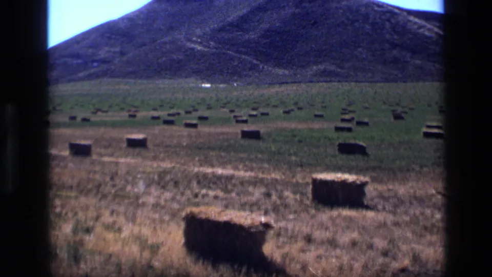 1972 Idaho 8mm frame showing scattered rectangular hay bales across dry grassland with a large mountain in the background.