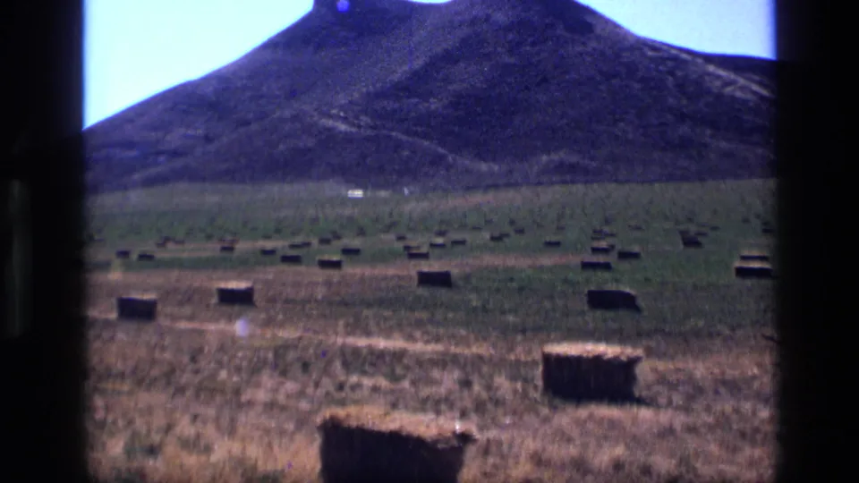 1972 Idaho rural landscape frame with hay bales spread across open grassland beneath a rounded mountain.