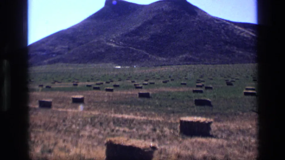 1972 Idaho 8mm frame showing a rural hay field with many square bales, dry grass, a dark hill, and visible film-gate edges.