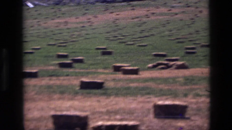 1972 Idaho 8mm frame with square hay bales in the foreground and midground, dry grass, green patches, and a partial hillside at top.
