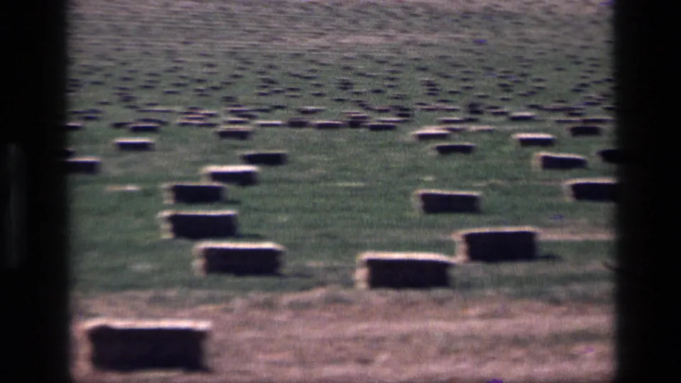 1972 Idaho 8mm frame with rectangular hay bales across green and dry grass, divided by dark foreground bars.