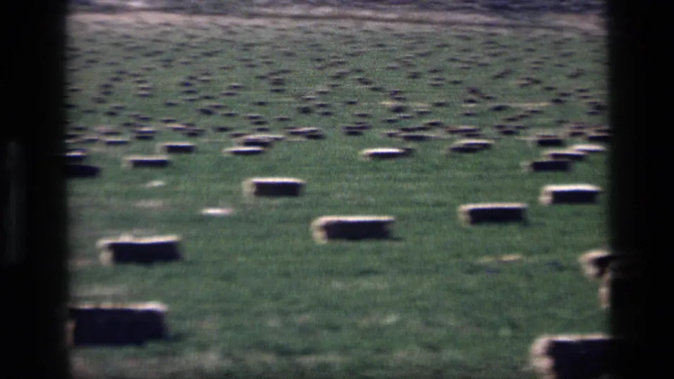 1972 Idaho 8mm view of scattered rectangular hay bales in a green field, with dark foreground framing at the center and edge.