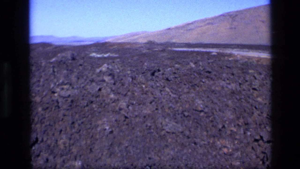 Rocky volcanic ground leading toward low hills and open sky.