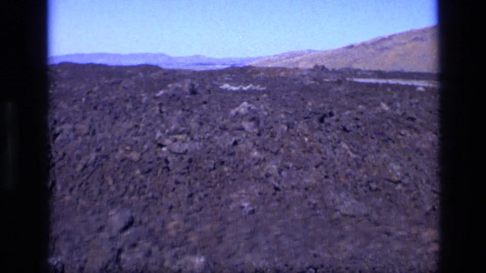 1972 Idaho home-movie frame of a barren lava field with distant ridgelines and faded color.