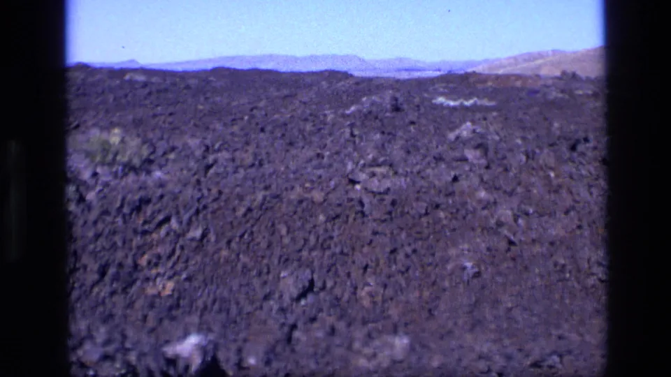 1972 Idaho 8mm view across a dark volcanic plain toward hazy mountains and blue sky.